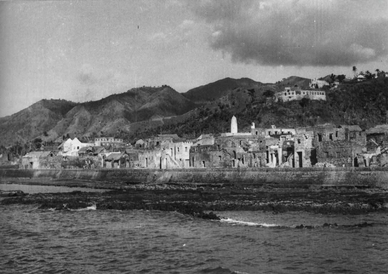Vue de la façade maritime de la ville de Mtsamɗu, à Ndzuani, dominée en hauteur par sa citadelle, photographiée en 1952. © Pierre Coudert/ECPAD